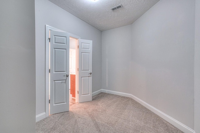 unfurnished room featuring a textured ceiling, carpet flooring, visible vents, and baseboards