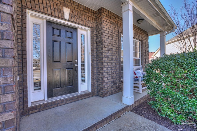 view of exterior entry featuring a porch and brick siding