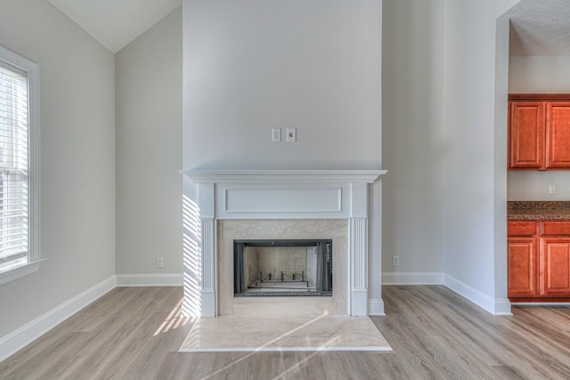 unfurnished living room featuring light wood finished floors, a high end fireplace, and baseboards