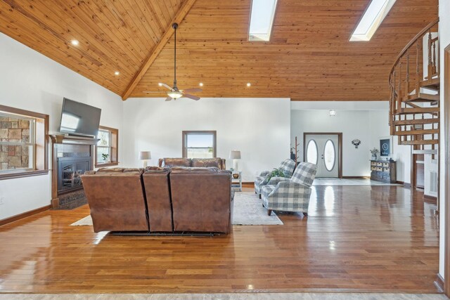 living area with a skylight, a glass covered fireplace, wood ceiling, wood finished floors, and high vaulted ceiling