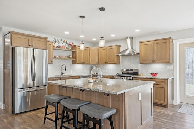 kitchen with a center island, stainless steel appliances, a sink, wall chimney range hood, and wood finished floors