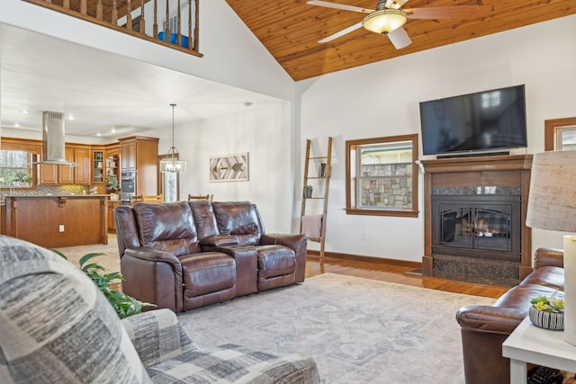 living room featuring light wood-style flooring, a glass covered fireplace, wood ceiling, high vaulted ceiling, and baseboards