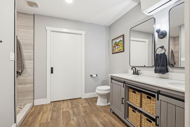 bathroom with double vanity, toilet, wood finished floors, a wall mounted air conditioner, and a sink