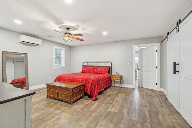 bedroom with a wall unit AC, light wood-style flooring, baseboards, and a barn door