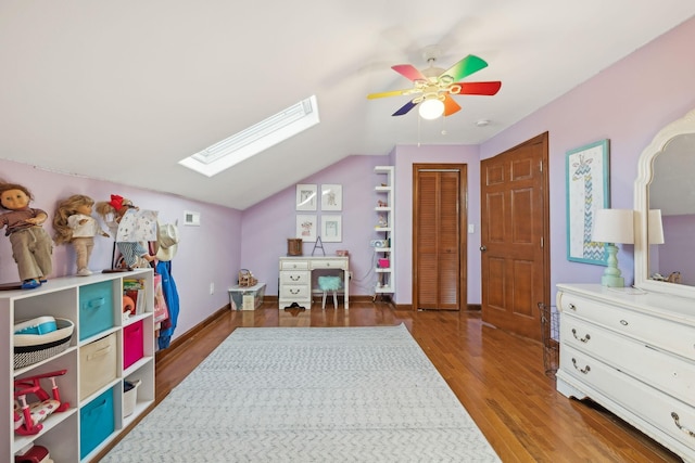 game room with vaulted ceiling with skylight, ceiling fan, baseboards, and wood finished floors