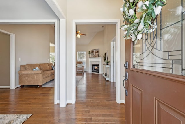 foyer entrance with wood finished floors, baseboards, a fireplace with flush hearth, ceiling fan, and vaulted ceiling