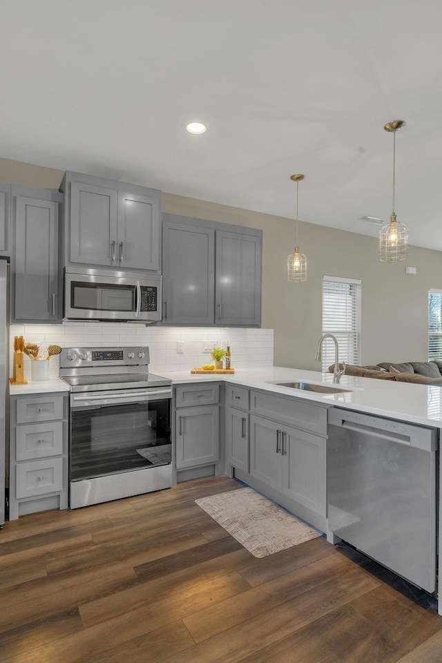 kitchen with decorative backsplash, appliances with stainless steel finishes, a peninsula, gray cabinetry, and a sink