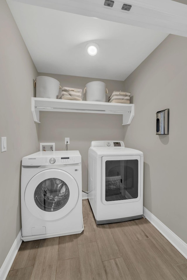 clothes washing area featuring laundry area, baseboards, separate washer and dryer, and wood finished floors