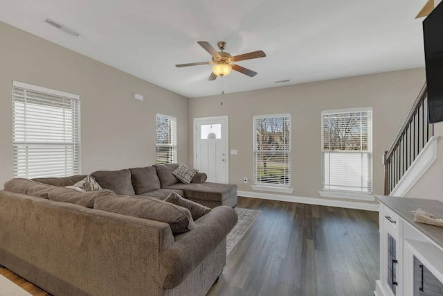 living area featuring baseboards, visible vents, ceiling fan, dark wood-style flooring, and stairs