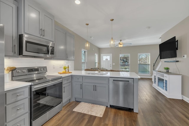 kitchen featuring a peninsula, appliances with stainless steel finishes, a sink, and gray cabinetry