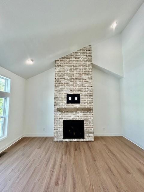 unfurnished living room featuring wood finished floors, visible vents, baseboards, vaulted ceiling, and a brick fireplace