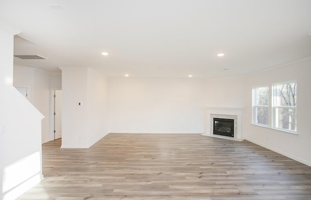 unfurnished living room featuring crown molding, light wood finished floors, a premium fireplace, and recessed lighting