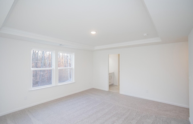 unfurnished bedroom with baseboards, a tray ceiling, ornamental molding, and light colored carpet