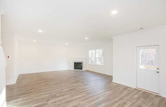 unfurnished living room with light wood-style floors, a fireplace with flush hearth, visible vents, and ornamental molding