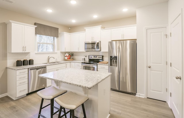 kitchen with light wood finished floors, appliances with stainless steel finishes, a sink, and a center island