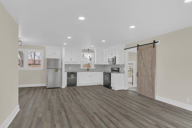 kitchen with stainless steel appliances, tasteful backsplash, a barn door, white cabinets, and a sink