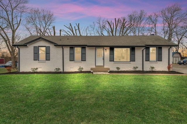 ranch-style home featuring crawl space, roof with shingles, a lawn, and brick siding