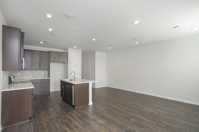 kitchen with a kitchen island with sink, dark wood-type flooring, a sink, open floor plan, and tasteful backsplash