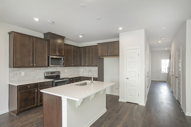 kitchen with dark brown cabinetry, dark wood-type flooring, a sink, stainless steel appliances, and backsplash