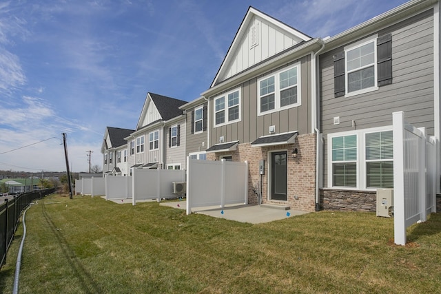 back of house featuring a yard, brick siding, board and batten siding, and fence