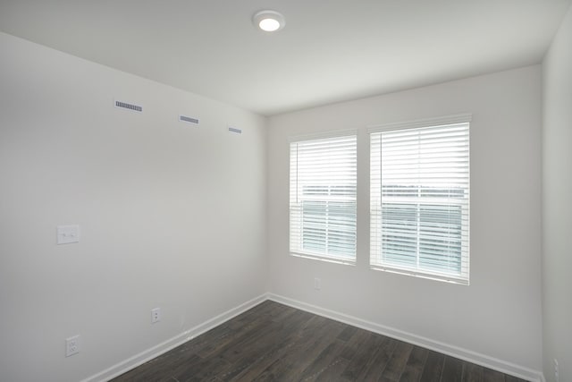 spare room featuring dark wood-style floors, visible vents, and baseboards