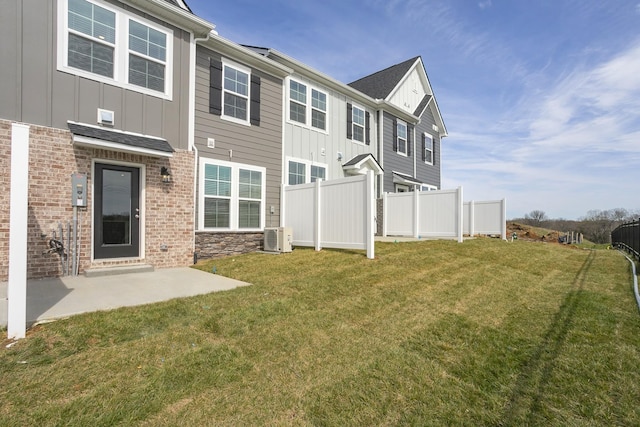 back of house featuring a yard, brick siding, board and batten siding, and fence