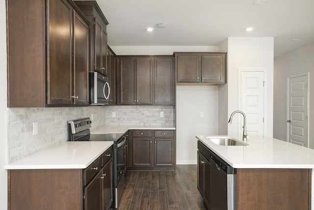 kitchen with dark wood-style flooring, a sink, appliances with stainless steel finishes, tasteful backsplash, and an island with sink