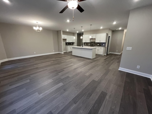 kitchen with ceiling fan with notable chandelier, white cabinetry, open floor plan, decorative backsplash, and an island with sink