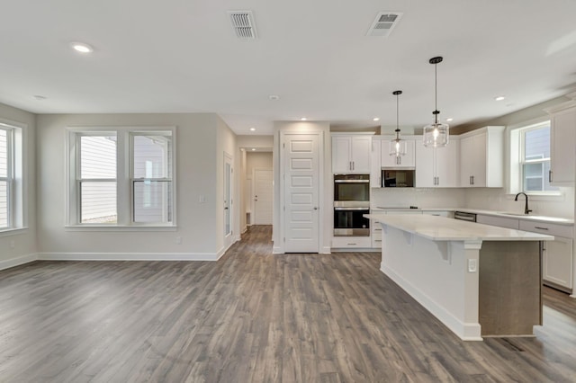 kitchen featuring visible vents, a sink, a center island, stainless steel double oven, and light countertops