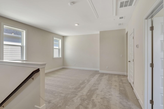 empty room featuring visible vents, baseboards, light colored carpet, and attic access