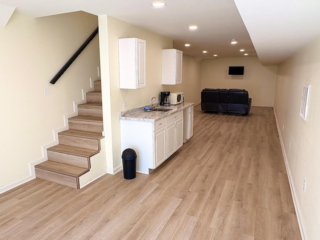 kitchen with light stone counters, light wood-type flooring, white cabinetry, a sink, and recessed lighting