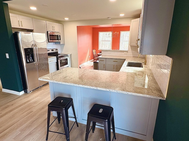 kitchen with appliances with stainless steel finishes, light wood-style floors, a peninsula, and light stone counters