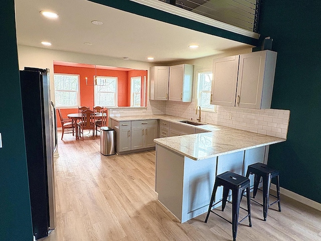 kitchen with a peninsula, light wood-style floors, a sink, and freestanding refrigerator