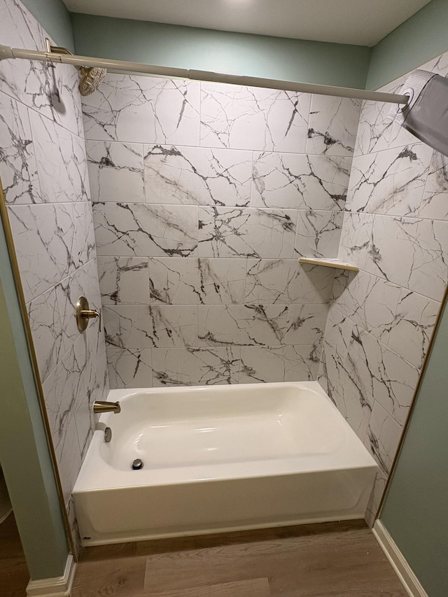 bathroom with washtub / shower combination, baseboards, and wood finished floors