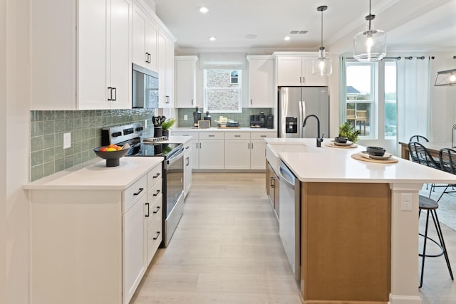 kitchen with a center island with sink, ornamental molding, a breakfast bar, stainless steel appliances, and a sink