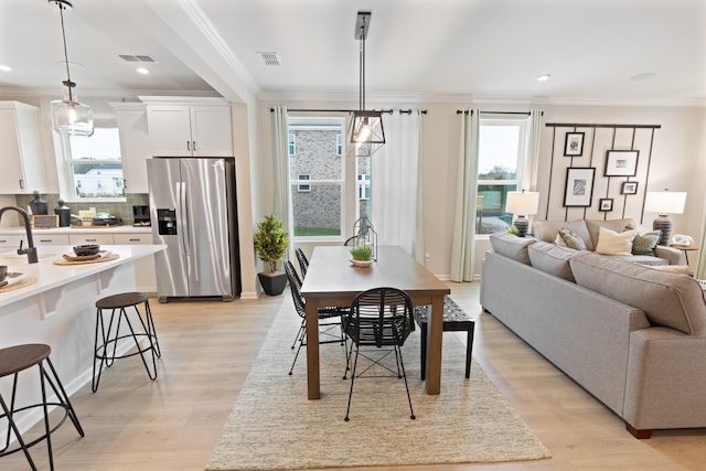 dining area featuring light wood-style floors, visible vents, and crown molding