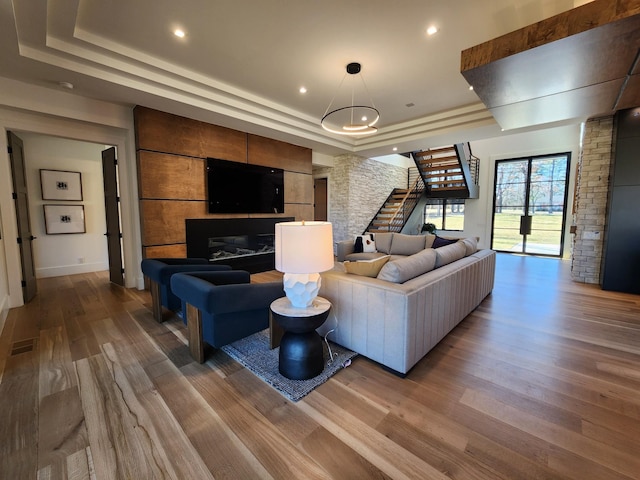 living area with wood finished floors, a raised ceiling, visible vents, and stairs