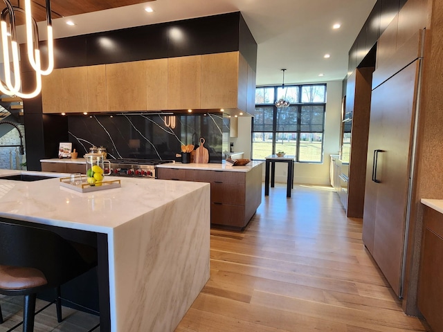 kitchen featuring a sink, hanging light fixtures, backsplash, light wood finished floors, and modern cabinets