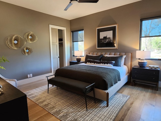 bedroom with ceiling fan, multiple windows, light wood-type flooring, and baseboards