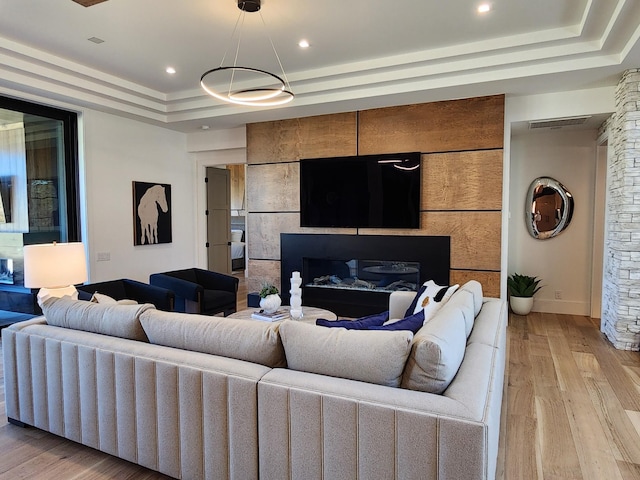 living room with light wood finished floors, visible vents, a tray ceiling, a fireplace, and recessed lighting