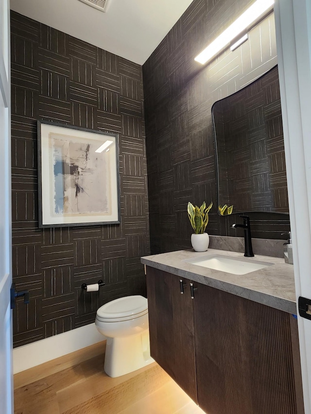 bathroom with toilet, wood finished floors, tile walls, and vanity