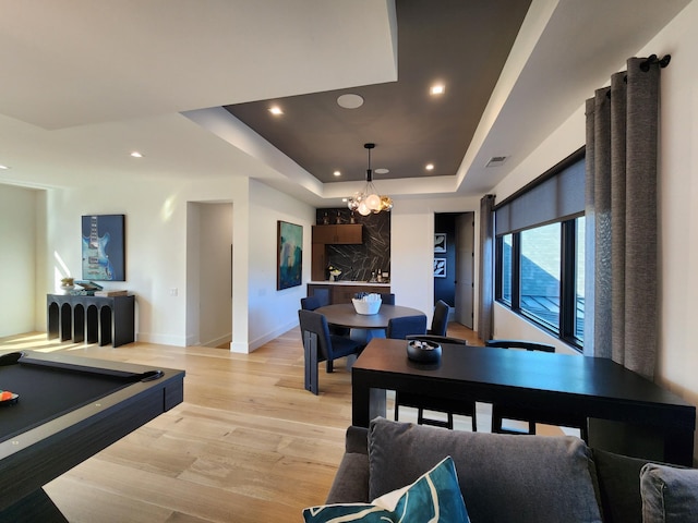 dining space featuring a notable chandelier, recessed lighting, a raised ceiling, light wood-style floors, and baseboards