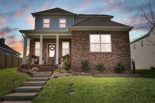 traditional-style house with covered porch, a yard, fence, and brick siding