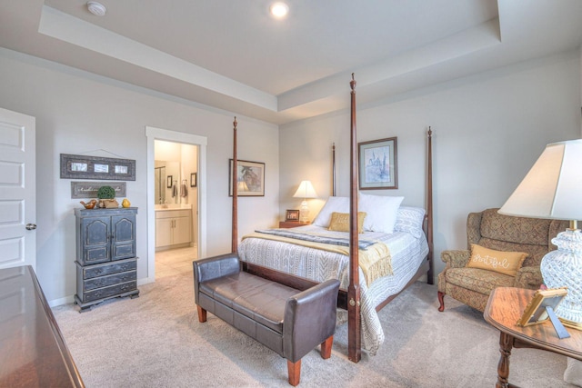 bedroom with baseboards, a tray ceiling, ensuite bathroom, and light colored carpet