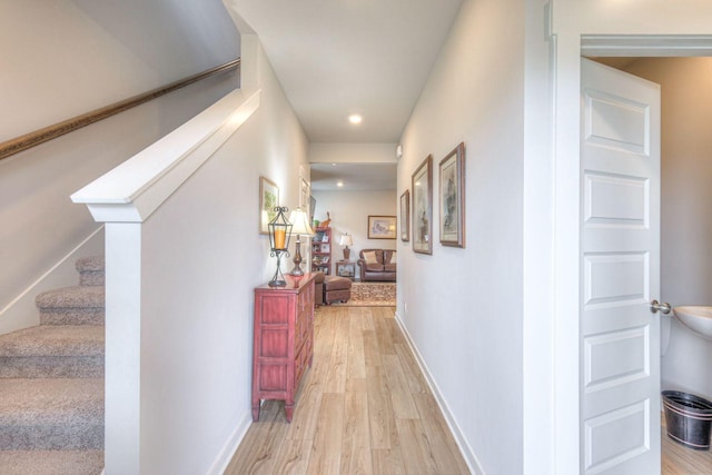 hallway with light wood-style floors, baseboards, and stairs