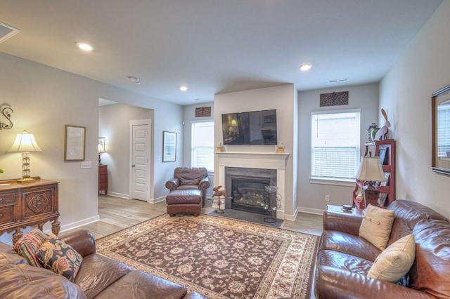 living room featuring plenty of natural light, visible vents, wood finished floors, and a fireplace with flush hearth