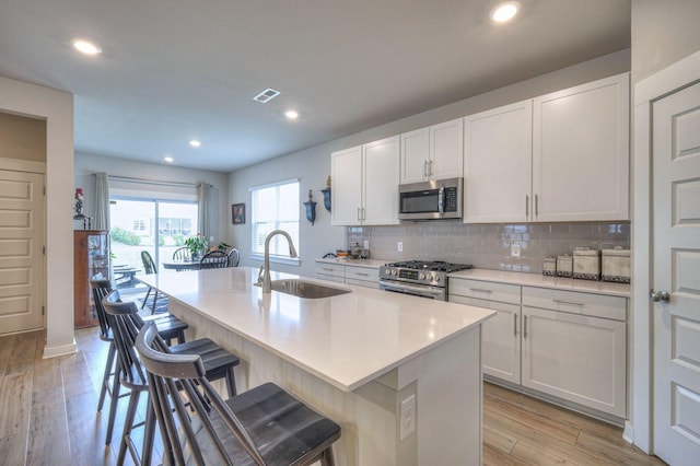 kitchen featuring a kitchen island with sink, a sink, visible vents, appliances with stainless steel finishes, and decorative backsplash