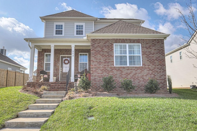 traditional-style home featuring covered porch, brick siding, a front lawn, and fence