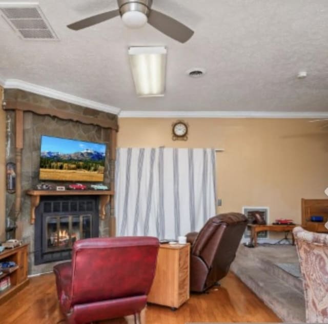 living room with crown molding, visible vents, wood finished floors, and a stone fireplace