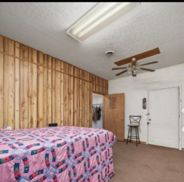 bedroom featuring wood walls, a textured ceiling, and carpet flooring